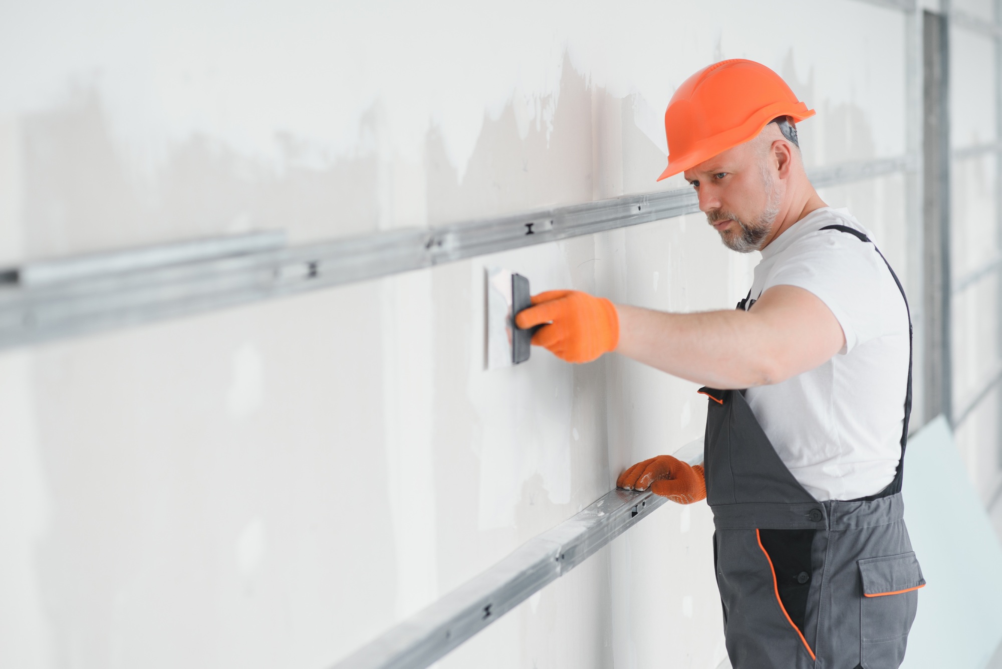 man drywall worker using trowel for plasterer putting stucco on plasterboard white wall.
